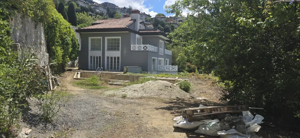 Tarihi binadaki villa projesinin gri cephesi, beyaz balkon korkulukları ve tadilat süren bahçesi