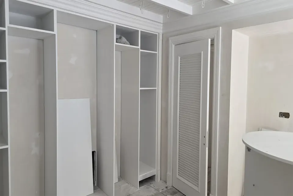 Kapakları takılmamış beyaz gardırop gövdesi ve yanında panjur kapı
