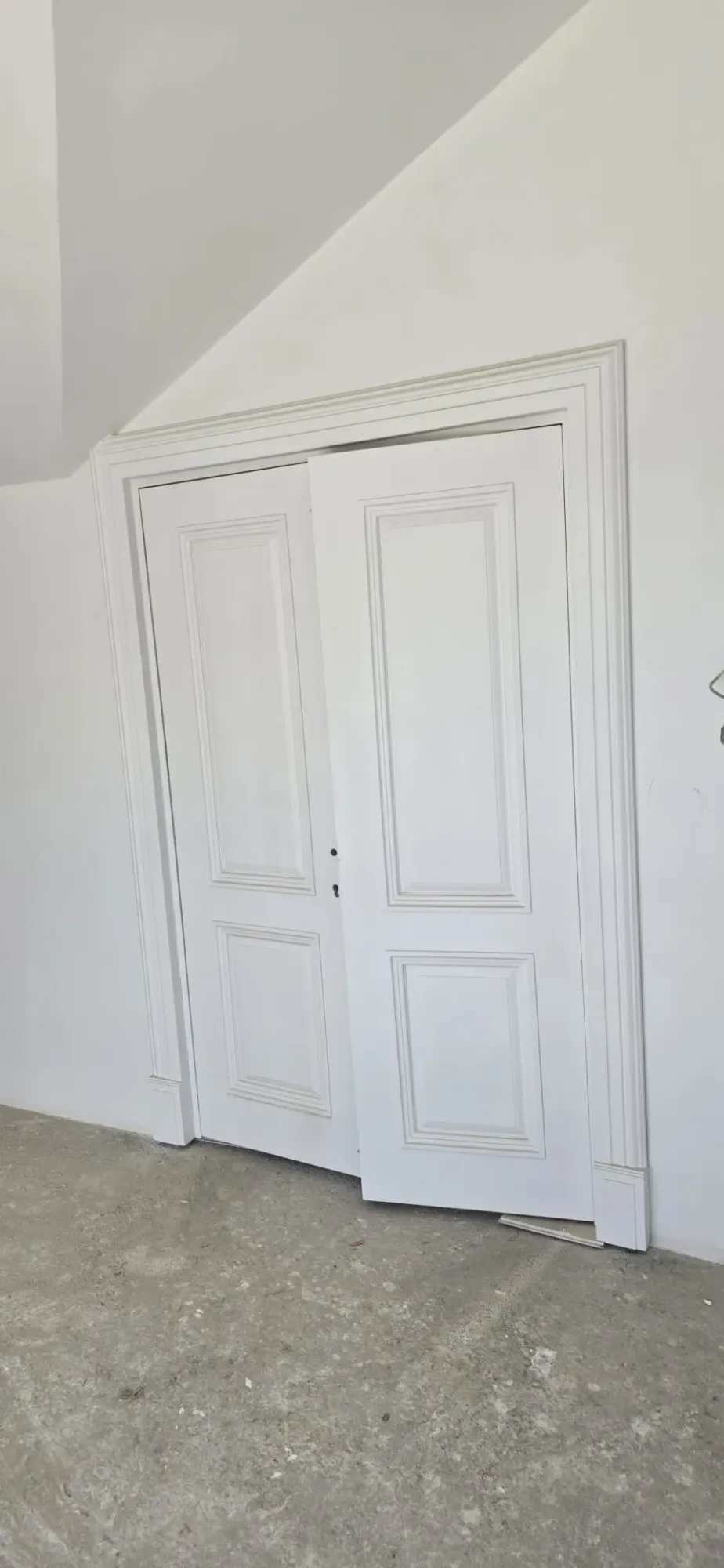 Eğimli tavan altında beyaz panelli çift kanatlı iç kapı ve profilli pervazı