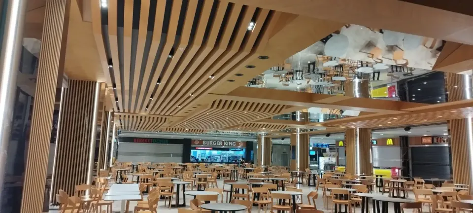 Geniş yemek alanında derinliğe doğru uzanan dalgalı ahşap çıtalar ve çıta kaplı kolonlar