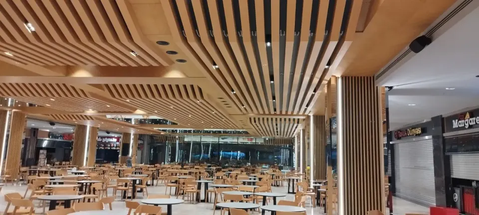 Spotlu ahşap çıta tavan, çıta kaplı kolon ve dükkan kepenkleri önünde boş masalar