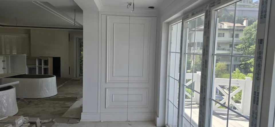 Villa salonunda pencere yanına yerleştirilen beyaz profilli çift kapaklı gömme dolap