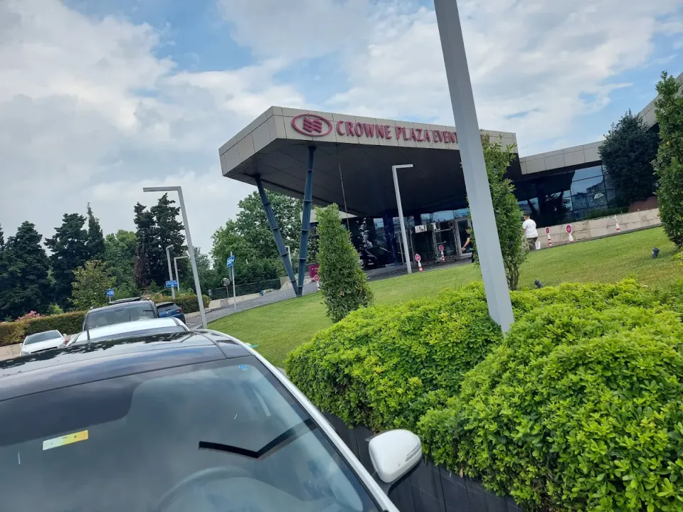 Otel yanmaz kapıları yazısında saçaklı otel girişi, bakımlı çimler ve park halindeki araçlar