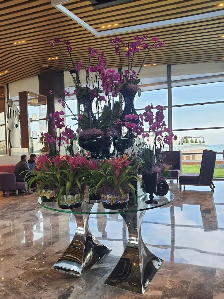 Otel lobisinde orkideli cam masa ve mor koltuklarla düzenlenmiş oturma alanı