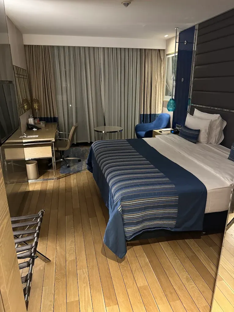 Beş yıldızlı otel odasında lacivert örtülü yatak, çalışma masası ve mavi koltuk