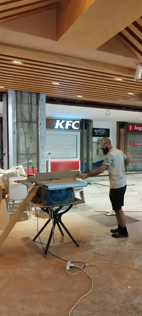Otel odası dekorasyonu hazırlığında çıtalı tavan altında tezgah testereyle kesim yapan usta